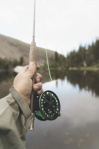 fishing rod shallow focus photography of person holding black and brown fishing rod casting